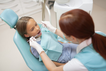 Top view of professional dentist examining schoolgirl