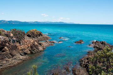 Kuaotunu beach from the north. Turquoise and blue water, rocky, great for snorkelling. Pohutukawa, NZs christmas tree. Summer scene, beautiful day, Coromandel is paradise. Postcard perfect sunny day.