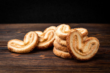 Palmier cookies or puff pastry ears on dark wooden background.