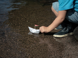 Kleiner Junge setzt Papierschiff ins Wasser