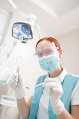 Fototapeta na wymiar Red-haired professional female dentist in a mask working hard
