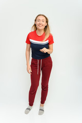 Full length studio portrait of a pretty young happy blonde woman in a tracksuit on a white background. He smiles, talks, shows with his hands, moves, shows emotions.