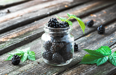 Fototapeta na wymiar Blackberry berries in a small glass jar and leaves on an old wooden table.
