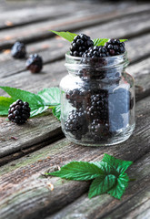 Fototapeta na wymiar Blackberry berries in a small glass jar and leaves on an old wooden table.