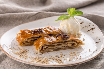 Traditional arabic dessert baklava with walnuts, honey and ice cream on white plate on grey tablecloth