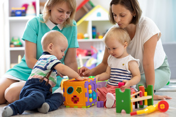 Group of babies play together with mothers in the classroom in nursery or preschool