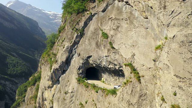 Aerial, drone shot, of a electric SUV car, driving in tunnels, close to a steep mountain wall, on a dangerous road, the Route de Derborence, on a sunny, summer day, in Sion, in the alps of Switzerland