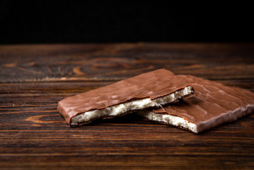 Chocolate bar with coconut filling on dark wooden background.