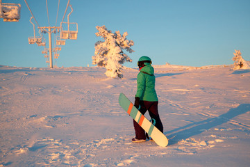 Joyful snowboarders, with snowboards in their hands, go up the mountain slope, amidst huge...
