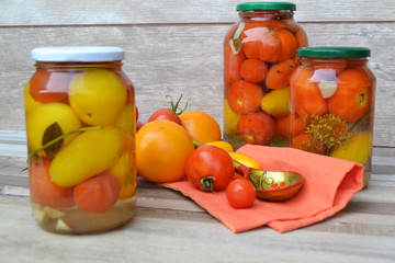 Preserved red and yellow tomatoes in a glass jar in russian traditional cuisine, spoon khokhloma and shabby background