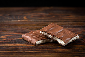 Chocolate bar with coconut filling on dark wooden background.