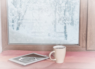 stands on the windowsill of a winter coffee window with a tablet and headphones, with a filter