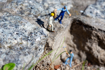 Miniature worker carrying a sand bag on a construction site while an instructor giving orders and another worker working in the quarry