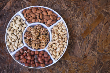 Nuts are part of a healthy diet . Set of nuts - walnut , cashew , peanuts , hazelnuts , almonds on a plate divided into portions . On a brown textured background.