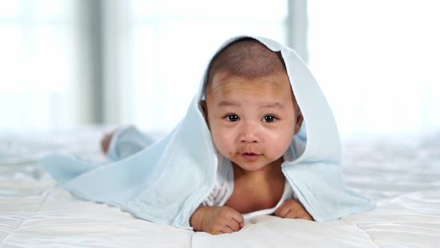 slow-motion of happy baby lying on bed under blanket in a bedroom