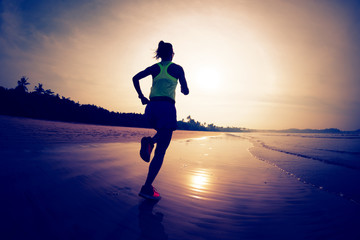 Sporty fitness woman runner running on sunrise beach