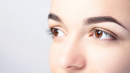 Woman with beautiful eyebrows close-up on a light background with copy space. Microblading, microshading, eyebrow tattoo, henna, powder brows concept