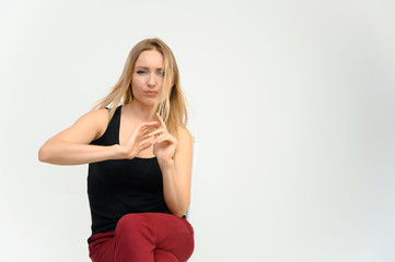 Studio waist-length photo portrait of a pretty beautiful young happy blonde woman with long hair on a white background in a black t-shirt and red trousers. Sits on a chair, smiles, shows emotions.