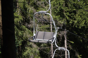 Emtpy double chair lift ride in sunny summer day. travel concept. backdrop of a dense forest....