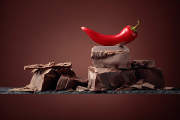 Black chocolate with red pepper on a brown background.