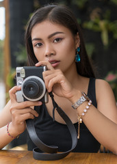 Asian girl  in a cafe looking on moment photo and hold camera.