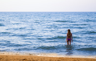 Young slender beautiful girl in bikini comes into the sea to swim