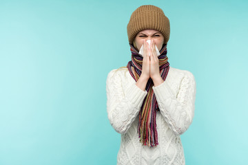 Health and medicine concept - Young woman blowing nose into tissue, on a blue background. Pretty...