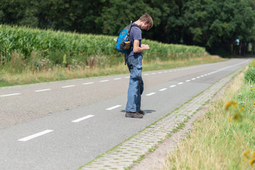 Fototapeta premium Young man with backpack on country road in summer.