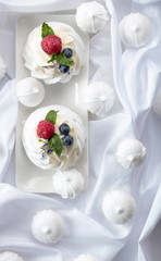 Dessert Pavlova with raspberries, blueberries and mint on a white fabric.