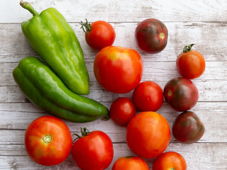 Green peppers and tomatoes of different shapes and sizes on wooden surface