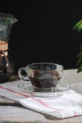 Drip brewing coffee concept. Wooden desk with chocolate cake and cup of coffee on black background.