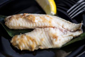 fried sea fish perch fillet with lemon on a plate on a dark background