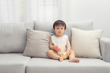 Fototapeta premium Little girl sitting and playing toy on the sofa in the living room. Kid concept.