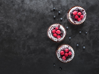 Three delicious tarts, colorful pastry cakes sweets with fresh raspberries and blueberry on black background.