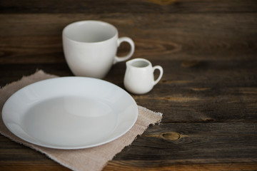 empty white plate with cup and ceramic jug on old wooden background