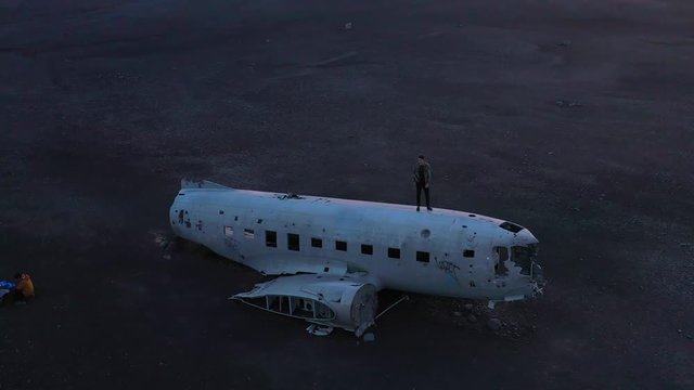 Aerial man standing on a crashed U.S. Navy DC-3 on the black sands of Solheimasandur, Iceland.