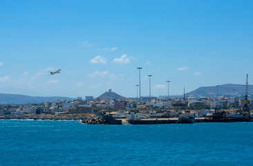 Airliner takes off over the port of Heraklion in clear weather on a hilly background with the command and control center - Powered by Adobe