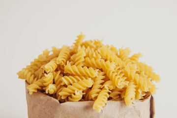 Spiral pasta in a paper bag on a white background. Copy, empty space for text