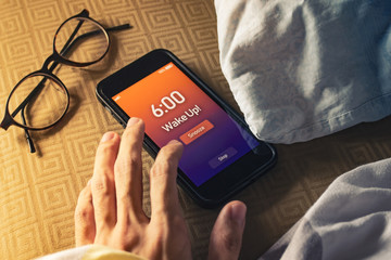 Men hand trying to snooze the alarm clock on smartphone.