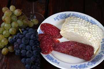 a glass of red wine, grapes, salami and soft cheese on a dark wooden table