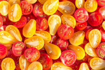 Fototapeta na wymiar Fresh halves of Mexican cherry tomatoes. Sliced yellow and red cherry tomatoes.Background of many colorful cherry tomatoes. Cherry tomatoes top view.