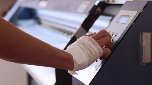 Worker in typography printing production on jet printer in printing office, hand closeup. Operator's hand turns on printing of industrial inkjet printing press with ciss system. Publishing industry.