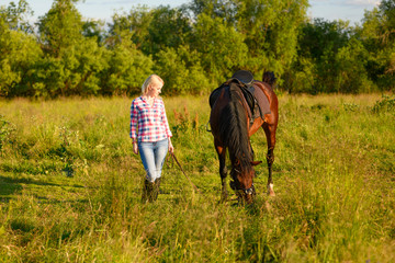 Naklejka na ściany i meble One Caucasian woman and her saddled bay trotter are on a pasture