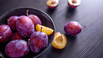 Fresh delicious plums in a plate on a black background