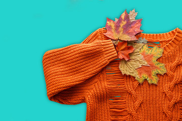 Orange sweater and autumn leaves isoalted over blue. Minimal style, flat lay