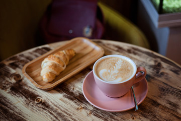 cup of coffee and croissant on wooden table