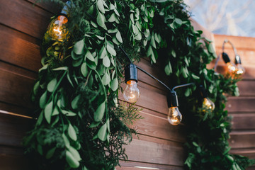 Garland with golden lights on green wreath on a wooden wall.