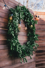 Garland with golden lights on green wreath on a wooden wall.