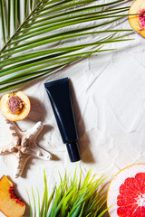 Safe sun. Skin care. A tube of cream lies on the beach sand, surrounded by vibrant fruits, corals,...