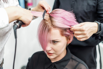 Fototapeta premium Hairdresser straightening pink hair with hair irons.